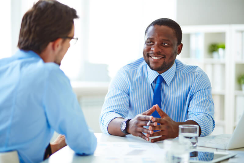 An African American man talking to a caucasian man in an office/business setting.